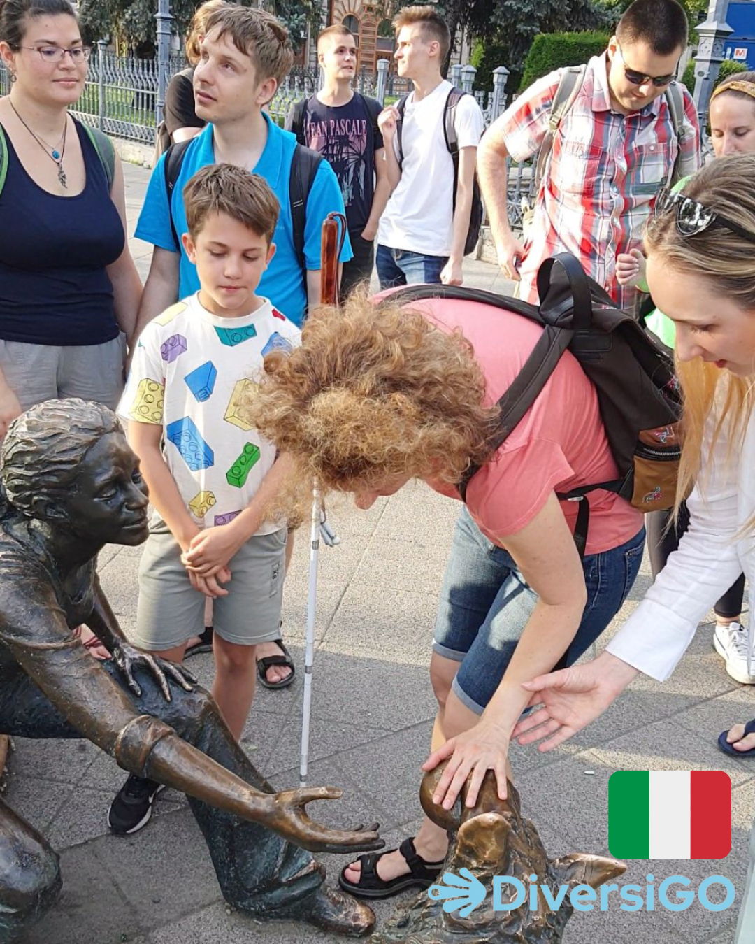 La guida di DiversiGO aiuta i turisti a osservare la statua tattile e realistica di una bambina che gioca con il suo cane.