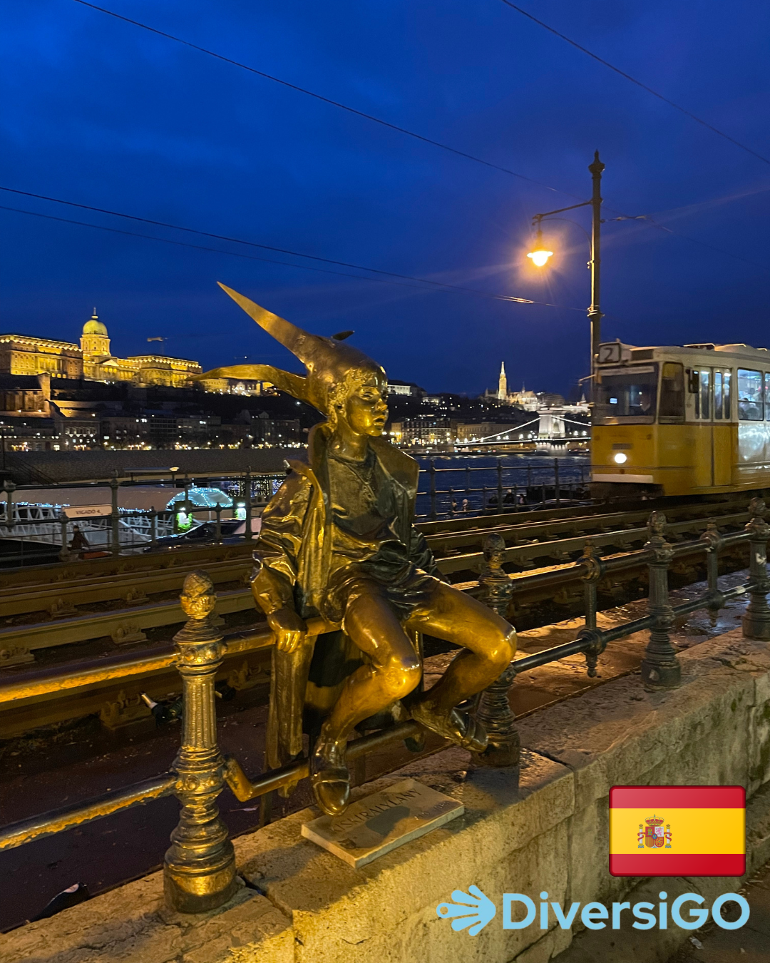 La popular escultura táctil de una niña vestida de princesa con accesorios caseros donde al fondo se ve el famoso tranvía 2 con el hermoso panorama a orillas del Danubio al atardecer.