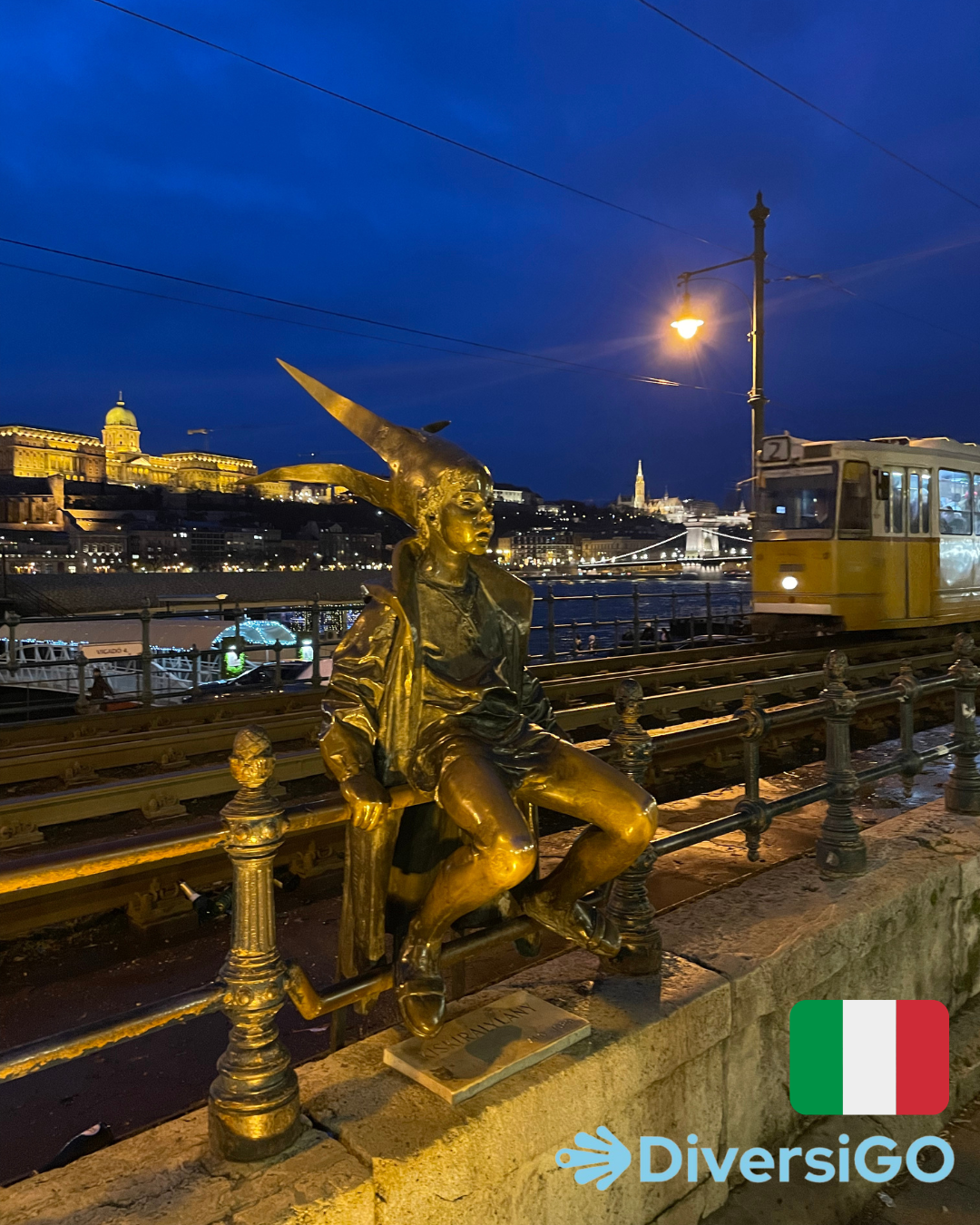 La popolare scultura tattile di una ragazza vestita da principessa che indossa accessori fatti a mano, sullo sfondo il famoso tram 2 con lo splendido panorama sulla riva del Danubio di sera.